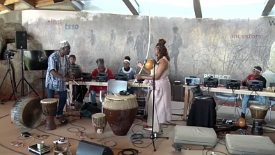 Musicians performing with traditional African drums and electronic instruments at !Khwa ttu San Heritage Center with a large poster backdrop