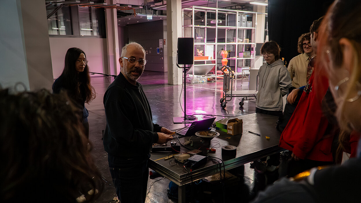 Dr. John Richards presenting at a table with electronic equipment during the Shifting Signals workshop at HfG Karlsruhe